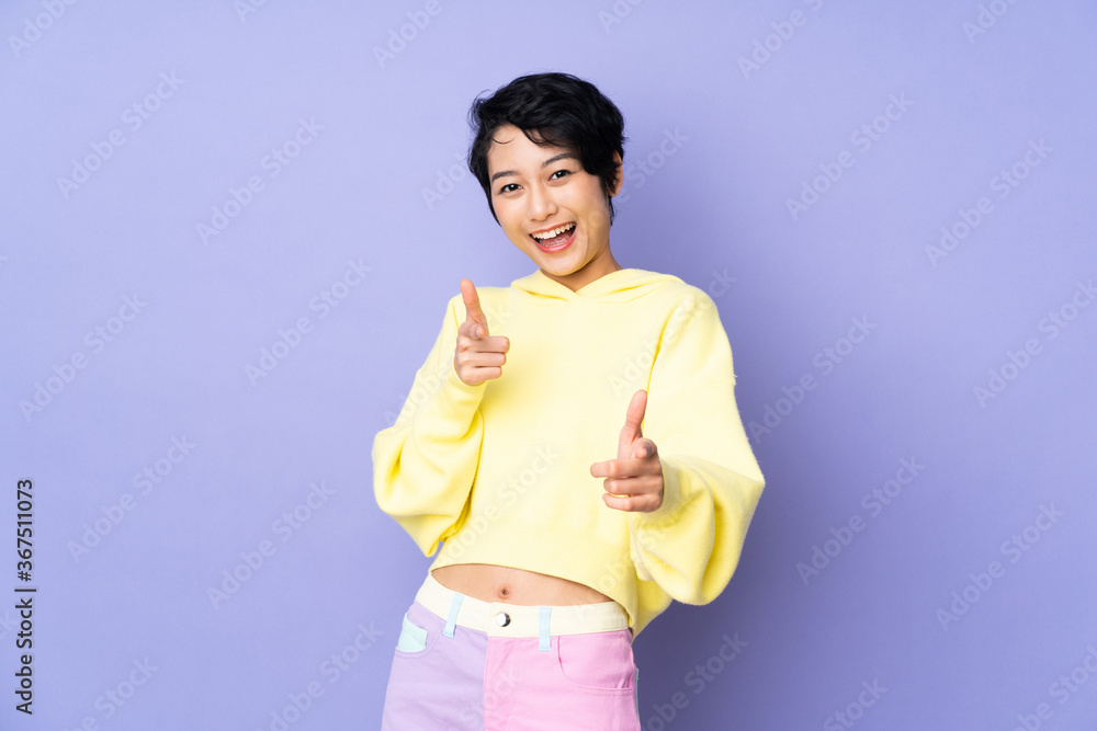 Young Vietnamese woman with short hair over isolated purple background pointing to the front and smiling Young Vietnamese woman with short hair over isolated purple background pointing to the front and smiling