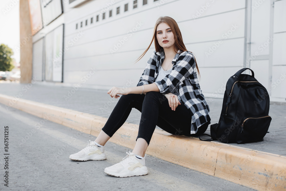 Young fashion woman sitting outdoors near gray background Young fashion woman sitting outdoors near gray background