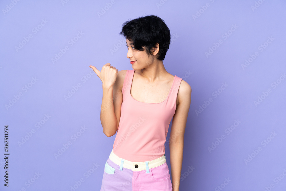 Young Vietnamese woman with short hair over isolated purple background pointing to the side to present a product Young Vietnamese woman with short hair over isolated purple background pointing to the side to present a product