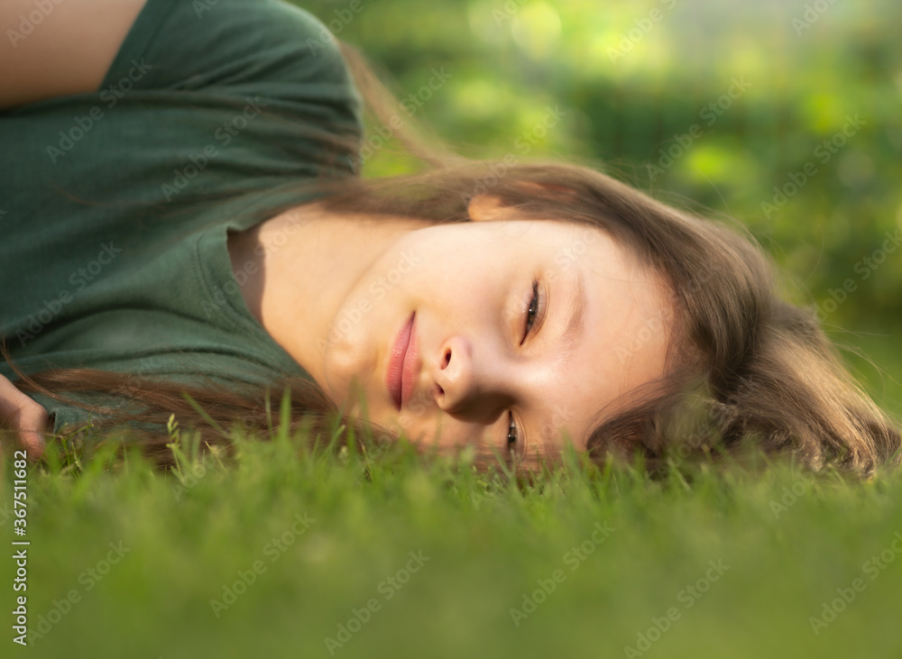 Happy smiling calm casual kid girl lying on the grass on nature summer background. Closeup Happy smiling calm casual kid girl lying on the grass on nature summer background. Closeup