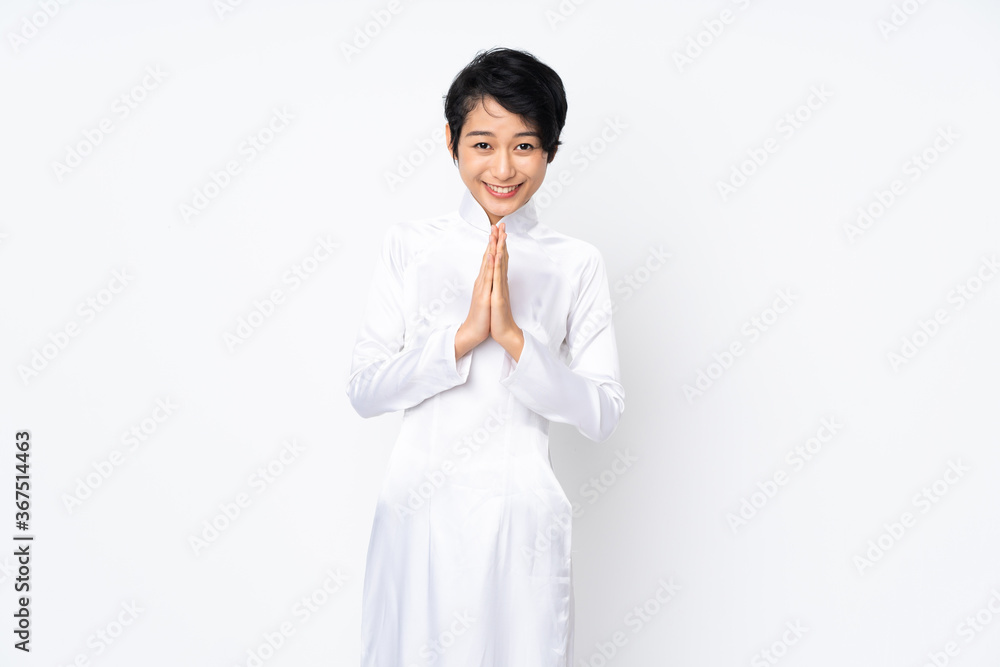 Young Vietnamese woman with short hair wearing a traditional dress over isolated white background keeps palm together. Person asks for something Young Vietnamese woman with short hair wearing a traditional dress over isolated white background keeps palm together. Person asks for something