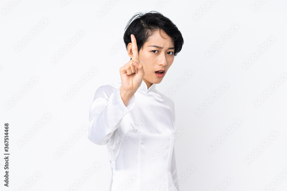 Young Vietnamese woman with short hair wearing a traditional dress over isolated white background counting one with serious expression Young Vietnamese woman with short hair wearing a traditional dress over isolated white background counting one with serious expression