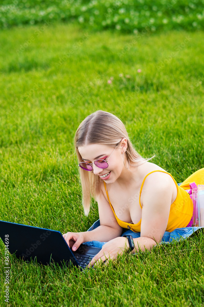Girl freelancer. Attractive woman using laptop lying on lawn in park surfing the net or preparing for exams. Technology, education and remote work concept. Freelance Worker. Girl freelancer. Attractive woman using laptop lying on lawn in park surfing the net or preparing for exams. Technology, education and remote work concept. Freelance Worker.