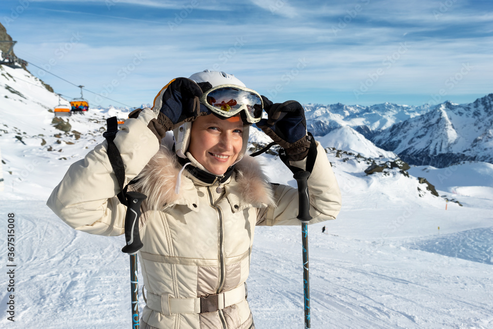 Young adult beautiful happy attractive caucasian smiling skier woman portrait teke on mask on mountain peak showing skiing resort panorama breathtaking view. Winter travel adventure welcome concept