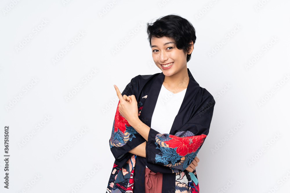 Young Vietnamese woman with short hair wearing a traditional dress over isolated white background pointing to the side to present a product Young Vietnamese woman with short hair wearing a traditional dress over isolated white background pointing to the side to present a product