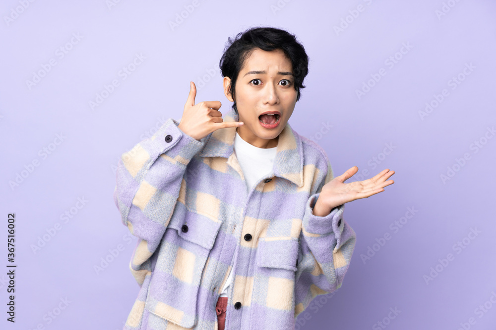 Young Vietnamese woman with short hair over isolated background making phone gesture and doubting Young Vietnamese woman with short hair over isolated background making phone gesture and doubting