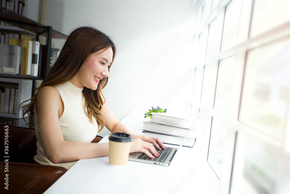 Woman using laptop with coffee by the window.