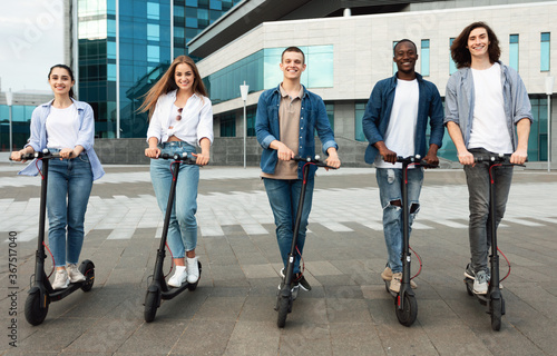 Happy friends having nice ride on motorized kick scooters