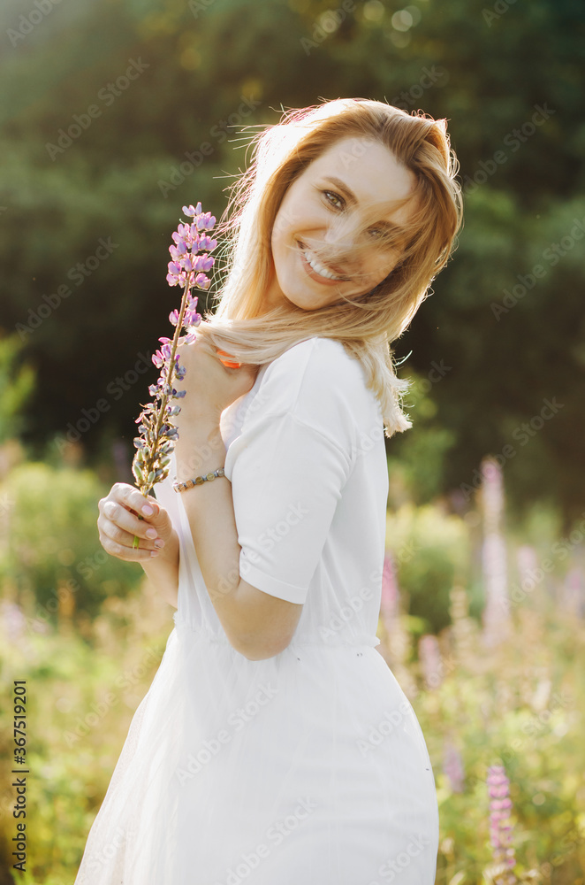 The wind blows the hair of a young blonde posing with a lupine flower in her hand. The wind blows the hair of a young blonde posing with a lupine flower in her hand.