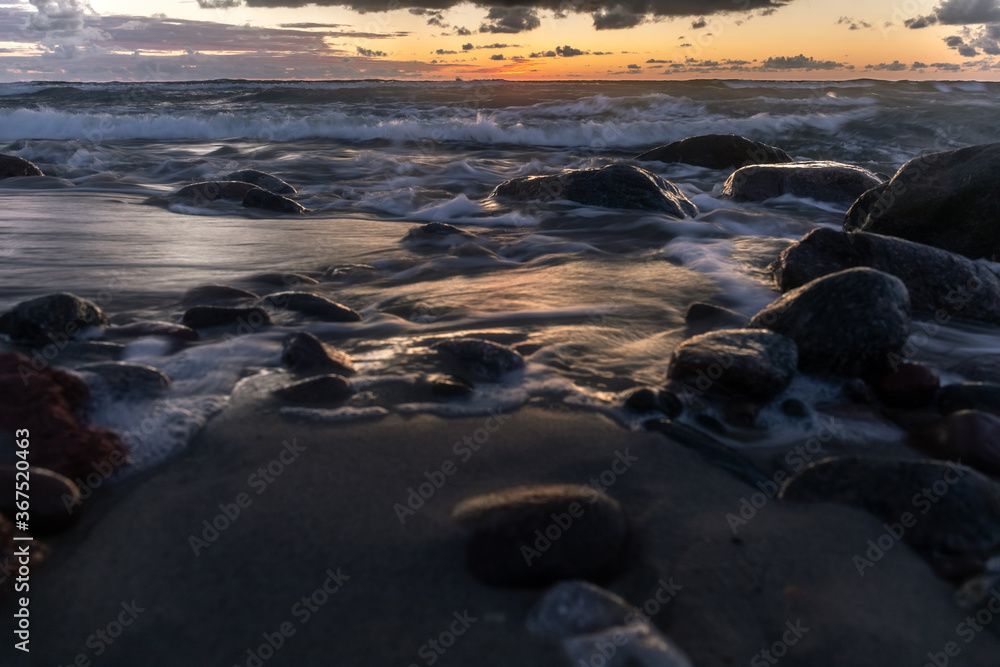 Obraz premium long exposure landscape, rocky ocean coastline with blurry waves in orange sunset light
