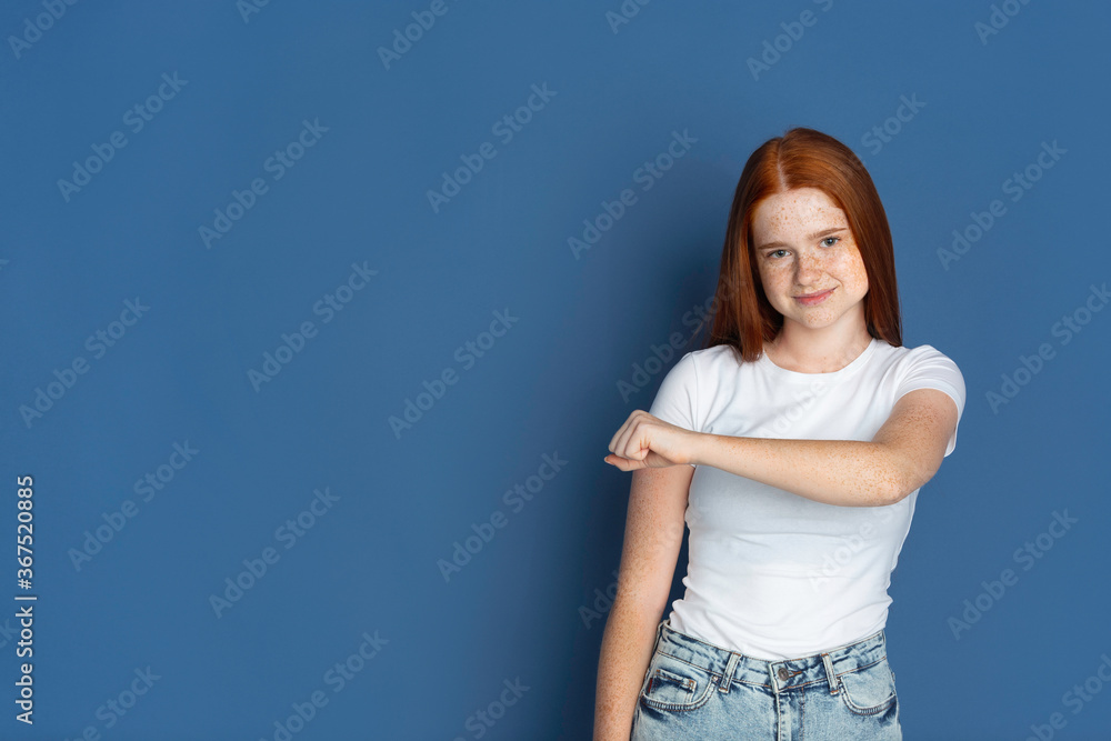 Fist bump. Caucasian young girl's portrait on blue background. Beautiful female redhair model with cute freckles. Concept of human emotions, facial expression, sales, ad, youth culture. Fist bump. Caucasian young girl's portrait on blue background. Beautiful female redhair model with cute freckles. Concept of human emotions, facial expression, sales, ad, youth culture.