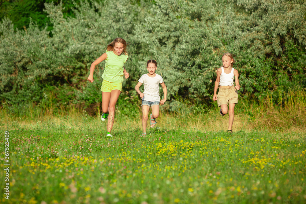 Obraz premium Kids, children running on meadow in summer's sunlight. Look happy, cheerful with sincere bright emotions. Cute caucasian boys and girls. Concept of childhood, happiness, movement, family and summer.
