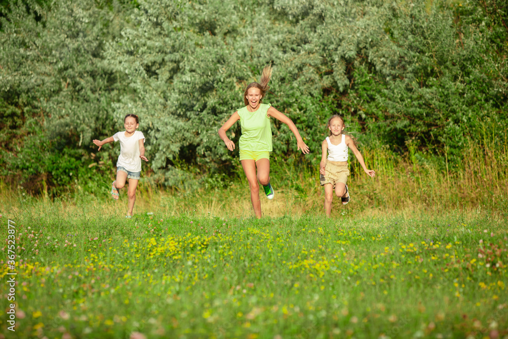 Obraz premium Kids, children running on meadow in summer's sunlight. Look happy, cheerful with sincere bright emotions. Cute caucasian boys and girls. Concept of childhood, happiness, movement, family and summer.
