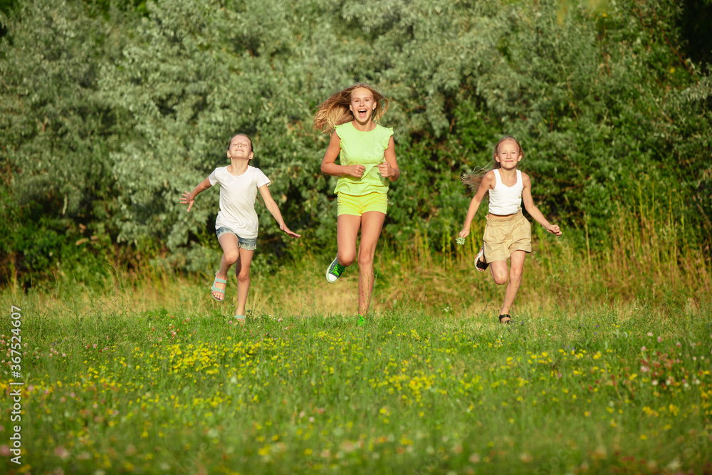 Kids, children running on meadow in summer's sunlight. Look happy, cheerful with sincere bright emotions. Cute caucasian boys and girls. Concept of childhood, happiness, movement, family and summer. Kids, children running on meadow in summer's sunlight. Look happy, cheerful with sincere bright emotions. Cute caucasian boys and girls. Concept of childhood, happiness, movement, family and summer.