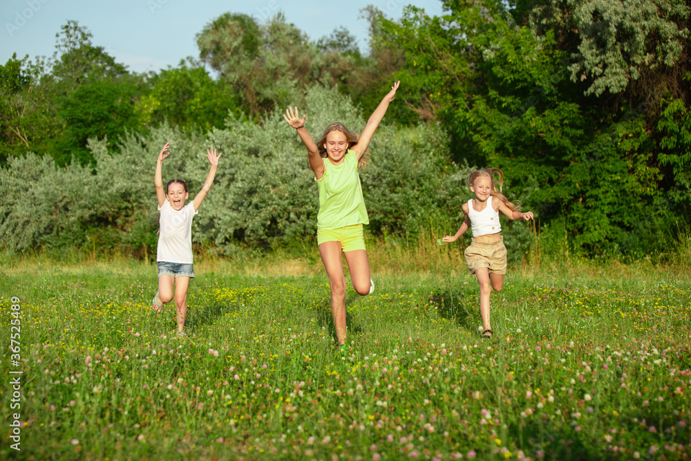 Obraz premium Kids, children running on meadow in summer's sunlight. Look happy, cheerful with sincere bright emotions. Cute caucasian boys and girls. Concept of childhood, happiness, movement, family and summer.