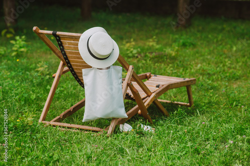 Photo Cotton wicker hat and eco bag near wooden deck chair