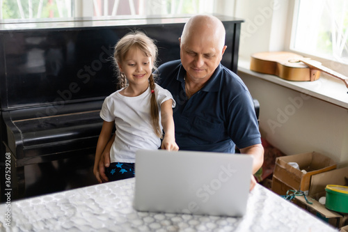Senior grandfather with small granddaughter indoors sitting at table.