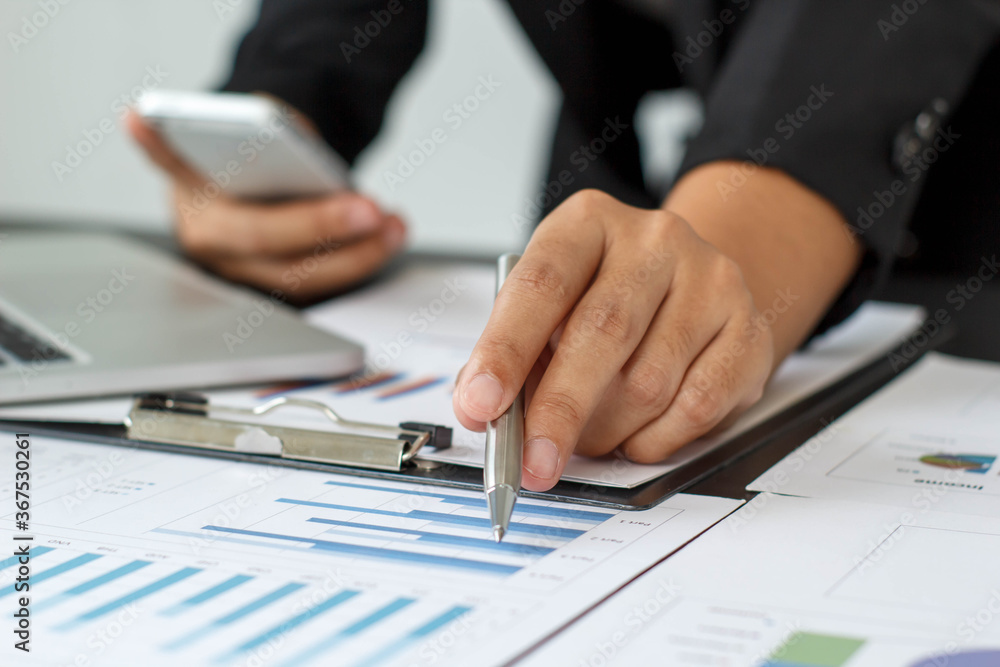 A businessman or accountant is sitting holding a pen to check the company's profit chart, the concept of growth planning in long-term investments. A businessman or accountant is sitting holding a pen to check the company's profit chart, the concept of growth planning in long-term investments.