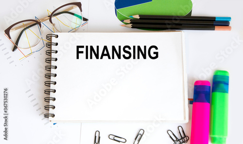 Text FINANSING on the page of a notepad lying on financial charts on the office desk. Near the calculator and marker. Business concept. photo