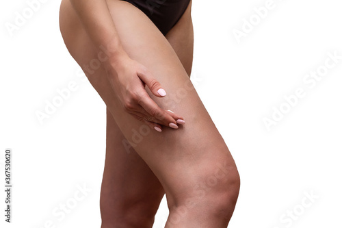 Crop photo of young woman applying cosmetic cream to her hip standing in the bathroom on white tile background. Close-up. Skin care concept.