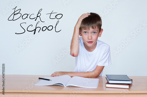 A cute boy is sitting at the table, a wound on the elbow. The child does not want to study, does not want to do homework