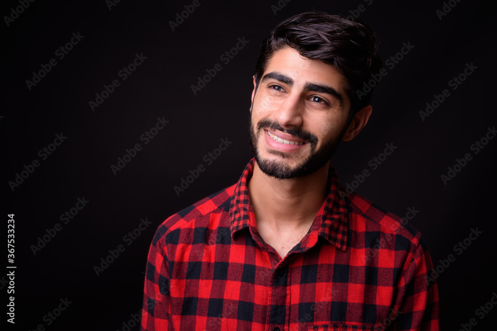 Young handsome bearded Persian man against black background