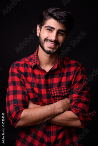 Young handsome bearded Persian man against black background
