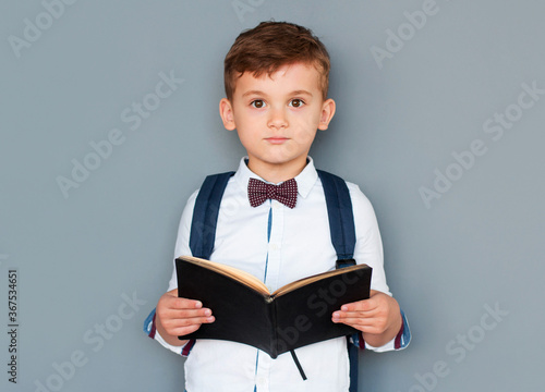 Cute little boy reading book on grey background