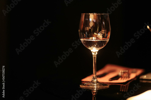 A glass of white wine on a glass table on a black background