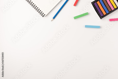 Colored wax crayons, sketchbook on white background. Colorful chalk. Flat lay, top view, copy space.