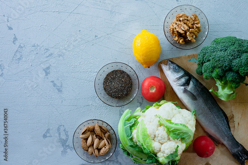 Fresh raw fish sea bass on cutting board, raw vegetables, spices and nuts. Stone background. Healthy food, lifestyle, diet and weight control concept. Space for a text. photo