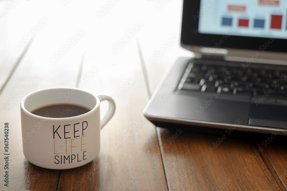 coffee cup with message keep life simple on a wooden table and a computer out of focus in the background coffee cup with message keep life simple on a wooden table and a computer out of focus in the background