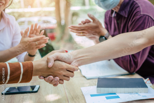 Group Asian businessmen and women shake hands together to create a mutually beneficial business relationship. The economic graph on the table