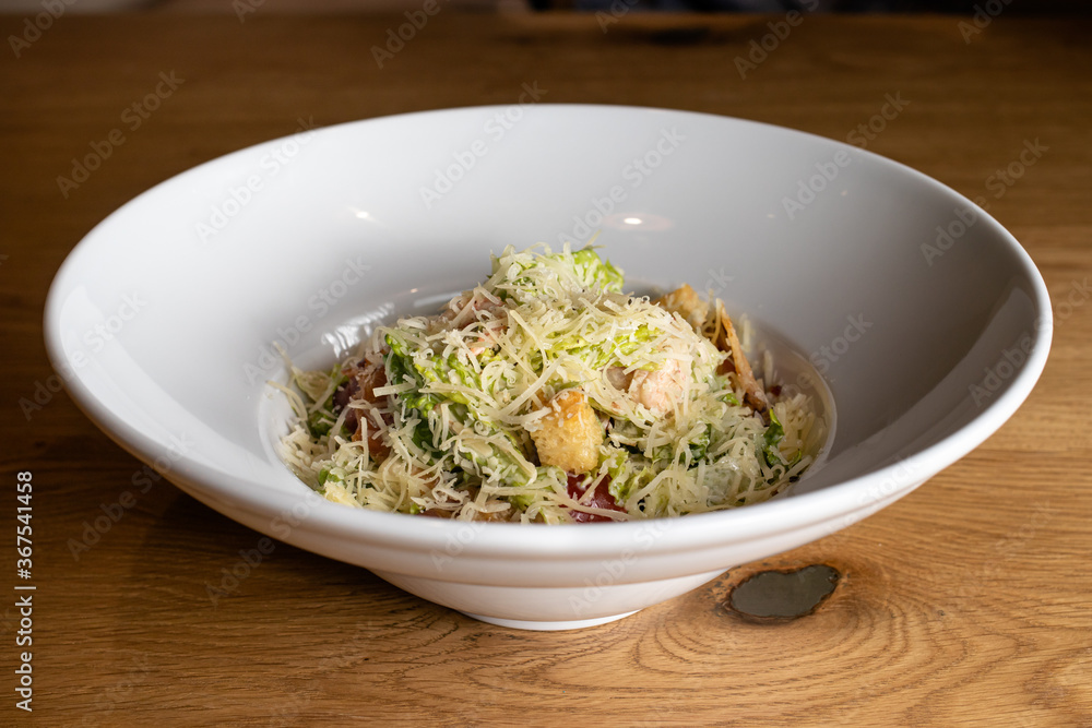 Salad with hard yellow cheese, herbs and chicken meat in a white plate. Restaurant menu