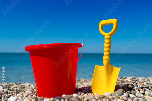 Toy bucket and spade on the beach stones Fototapet