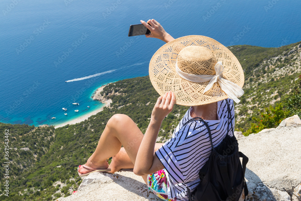 Fototapeta premium Active sporty woman on summer vacations taking selfie picture while enjoying beautiful coastal view of Cres island, Croatia from Lubenice traditional costal village.