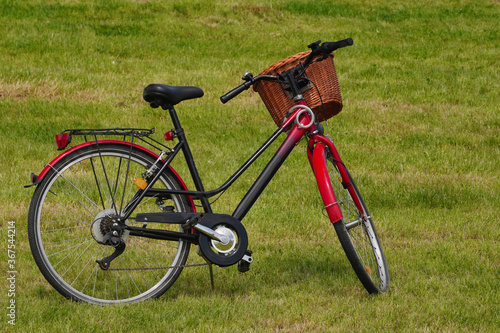 A red-and-black city Bicycle with a basket stands in a meadow, on the newly mown grass in the Park. Walking and driving in the fresh air in Sunny weather, an eco-friendly form of transport