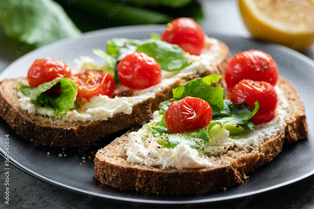 Toast with soft ricotta cheese, roasted tomatoes and lettuce garnished with olive oil and black pepper. Healthy gourmet italian bruschetta