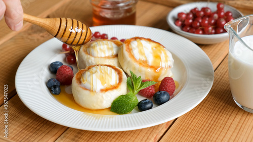 Pouring honey on cottage cheese fritters. Russian Ukrainian cuisine food Syrniki, sweet cheese fritters served with sour cream, berries and honey
