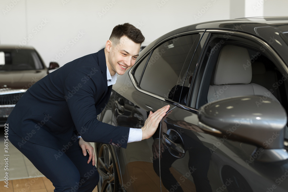 Handsome young businessman in classic blue suit is smiling while examining car in a motor show