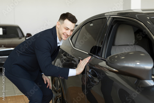 Handsome young businessman in classic blue suit is smiling while examining car in a motor show © Artem Zakharov