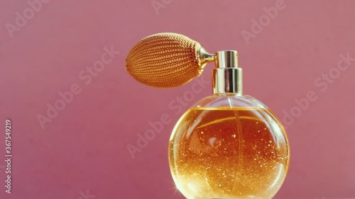 Luxury golden perfume bottle and shining light flares on pink background, glamorous fragrance scent as perfumery product for cosmetic and beauty brand, stock footage photo