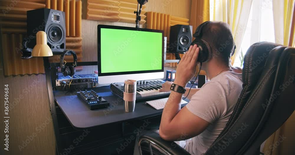 A man produce electronic music in home studio using headphones, play on midi keyboard and look in green screen on monitor A man produce electronic music in home studio using headphones, play on midi keyboard and look in green screen on monitor