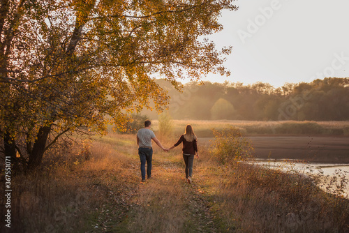A young man and a girl are walking in the autumn forest. Happy lovers hold hands, hug each other, kiss, spend time together. Traveling during the cold season, on weekend days. Couple in love forever © farmuty