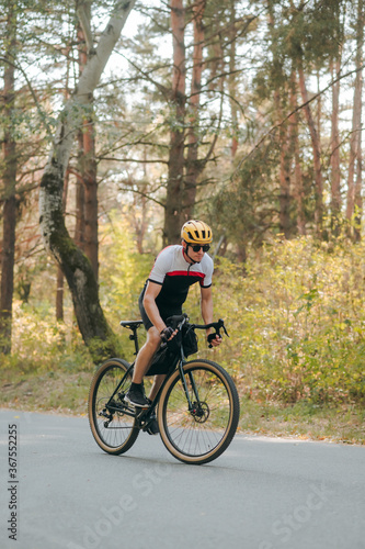 Professional cyclist in sports gear trains on a bicycle in the autumn forest. A man rides his bicycle on a country road in the fall season. Vertical photo.