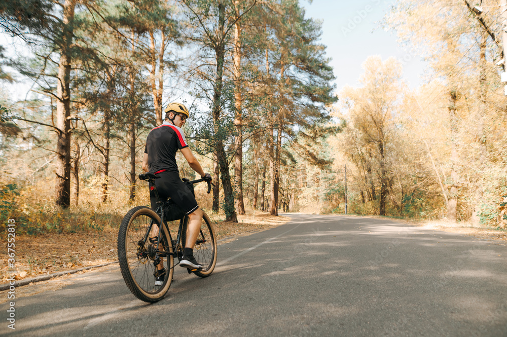 Cyclist stands with bicycle on road in autumn forest and rests. Professional cyclist in helmet and sportswear walking on a forest road. Copy space