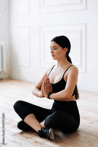 Meditation of a female athlete at home. The young woman sits on the floor with her legs crossed and her arms folded in front of her.