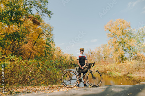 Male cyclist standing with bicycle on background of beautiful autumn landscape and looking into camera. A cyclist is on a bike ride through the autumn park. Outdoor activities.Cycling concept.