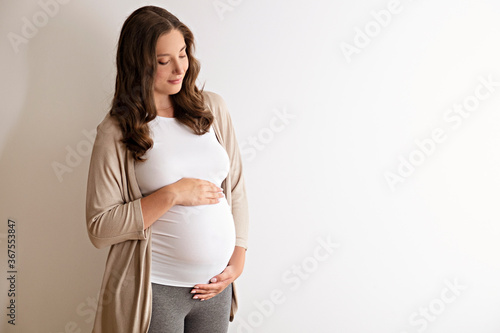 Portrait shot of young beautiful woman on third trimester of pregnancy. Close up of pregnant female with arms on her round belly. Expecting a child concept. Background, copy space. photo