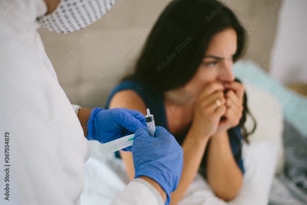 Scared young female getting an injection from a nurse in a face mask Scared young female getting an injection from a nurse in a face mask
